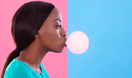 Woman blowing a chewing gum bubble against a pink and blue background