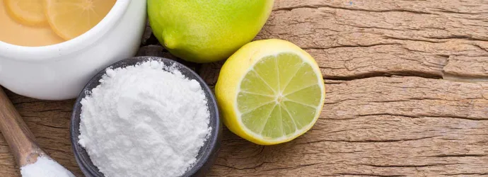 Eco friendly cleaning products such as a lemon, lime, and baking soda on a wooden chopping board