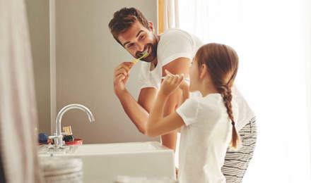 A man and his young daughter learning how to save water whilst brushing their teeth together in a bathroom