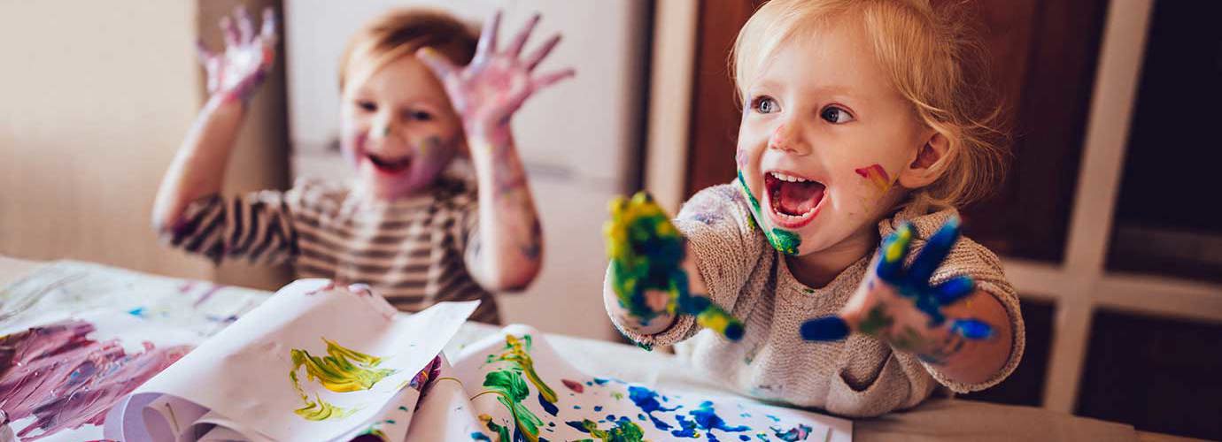 Twee kinderen spelen met hun rommelige handen met een kunstenaarspalet en blauwe verf
